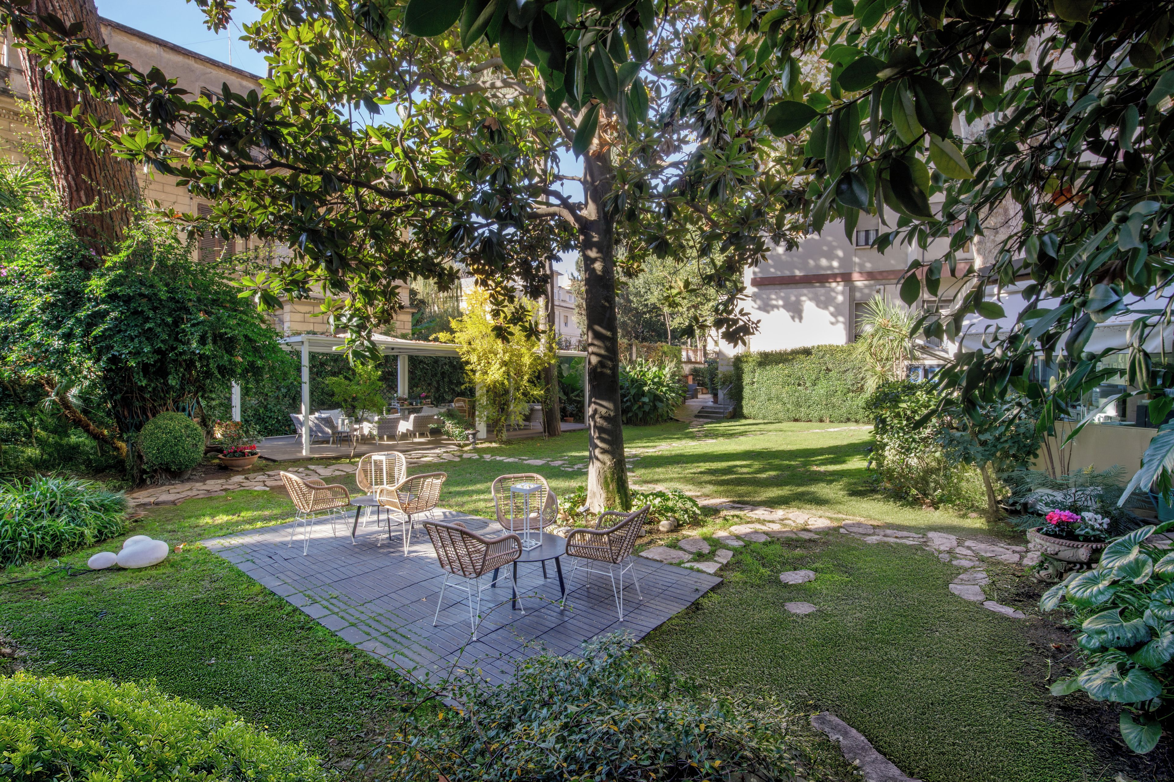 Ein Garten mit einer Terrassenanlage, Gartenmöbeln, einem gepflasterten Weg und üppiger Bepflanzung.