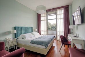 A hotel room with a bed, a desk, a chair, a TV, and a window with curtains. - Fenix Hotel (Rome)