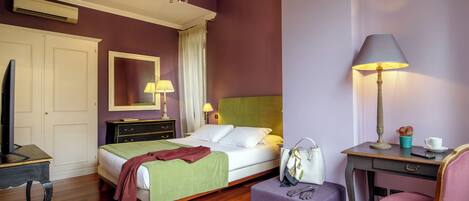 A hotel room with a bed, bedside table, chair, desk, and a mirror on the wall.