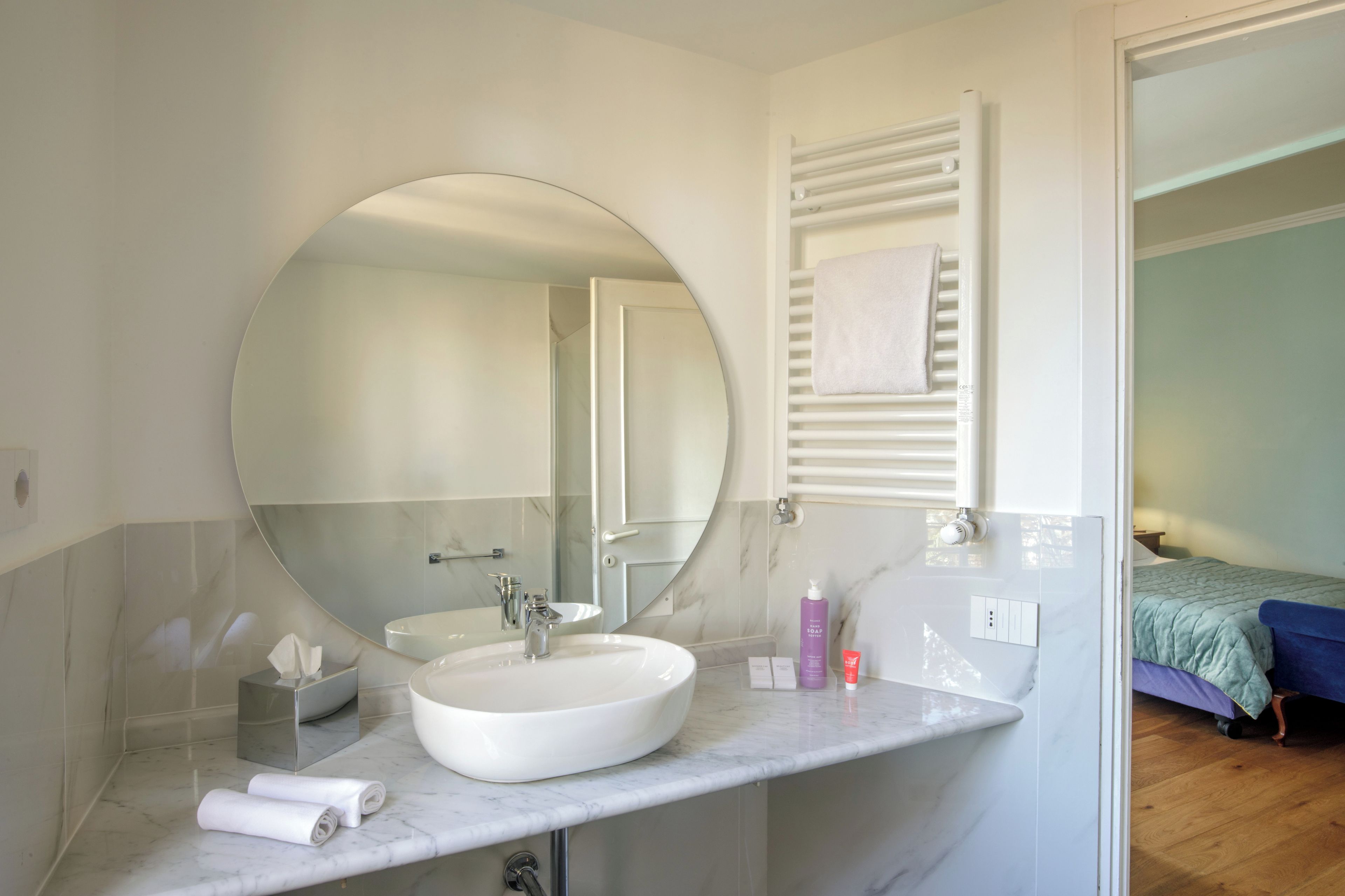 A bathroom with a round mirror, a sink, and a towel rack.