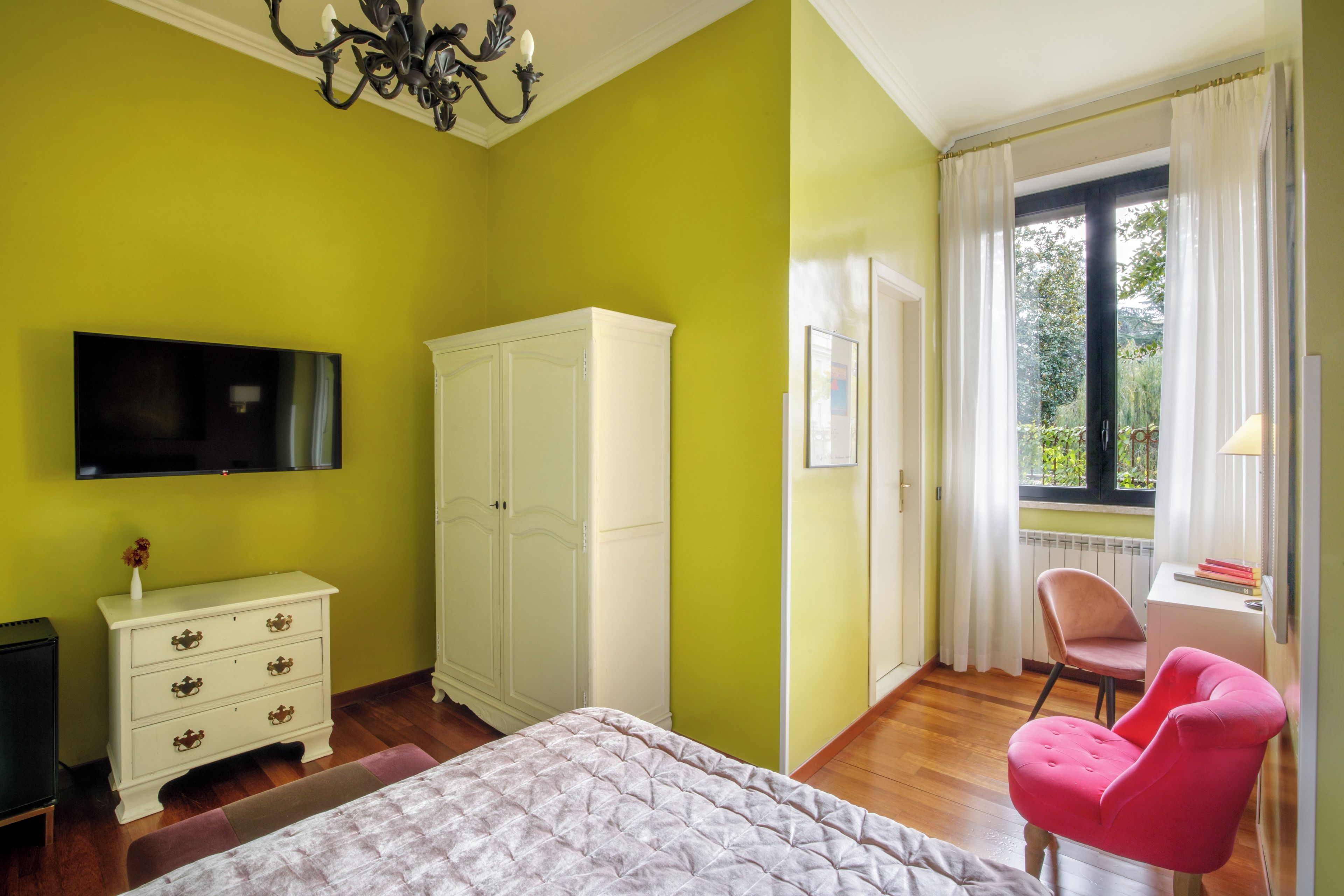 Una habitación con cama, televisión, armario, silla y ventana con cortinas.