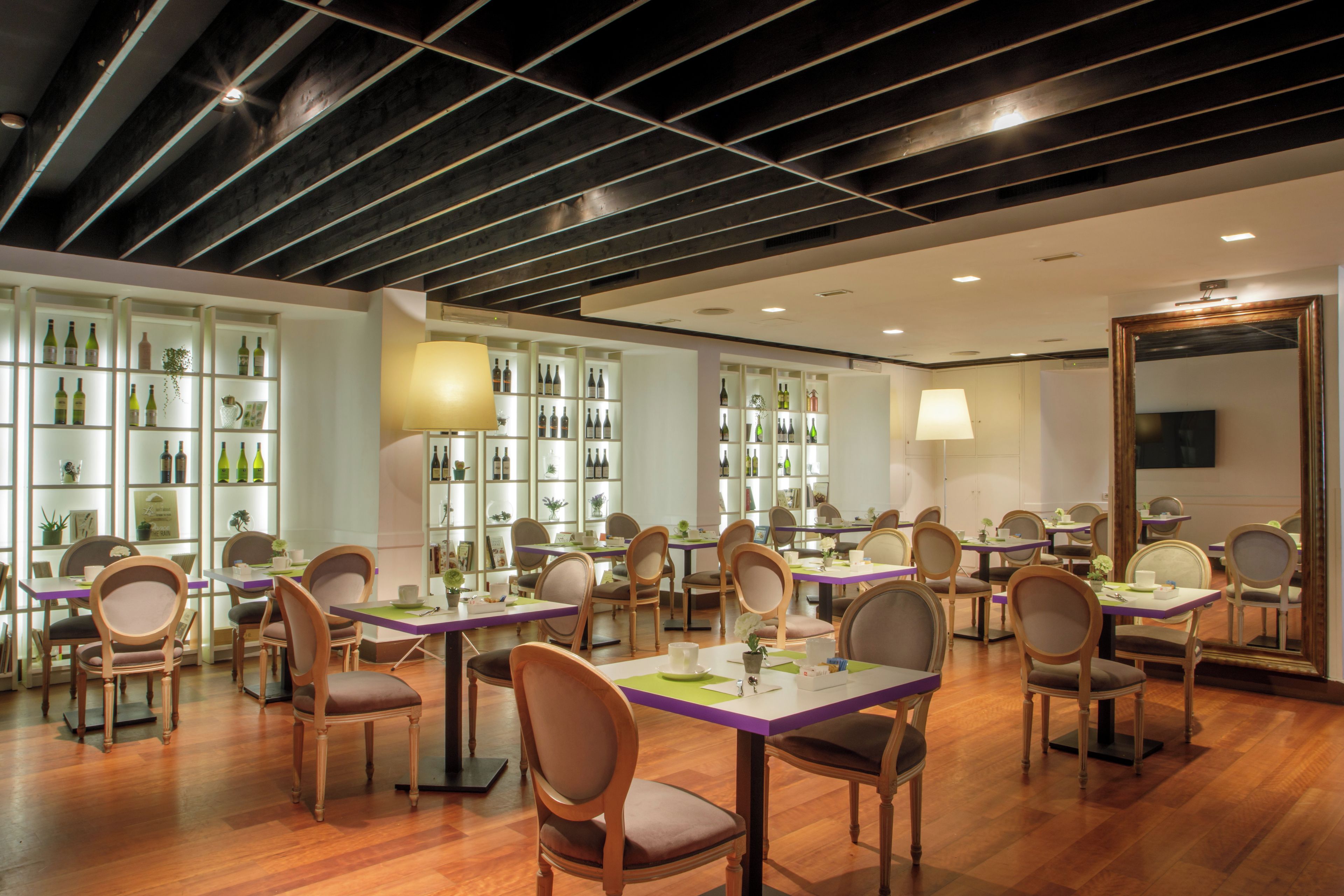 Interior de restaurante con suelo de madera, varias mesas con sillas y estanterías con botellas.