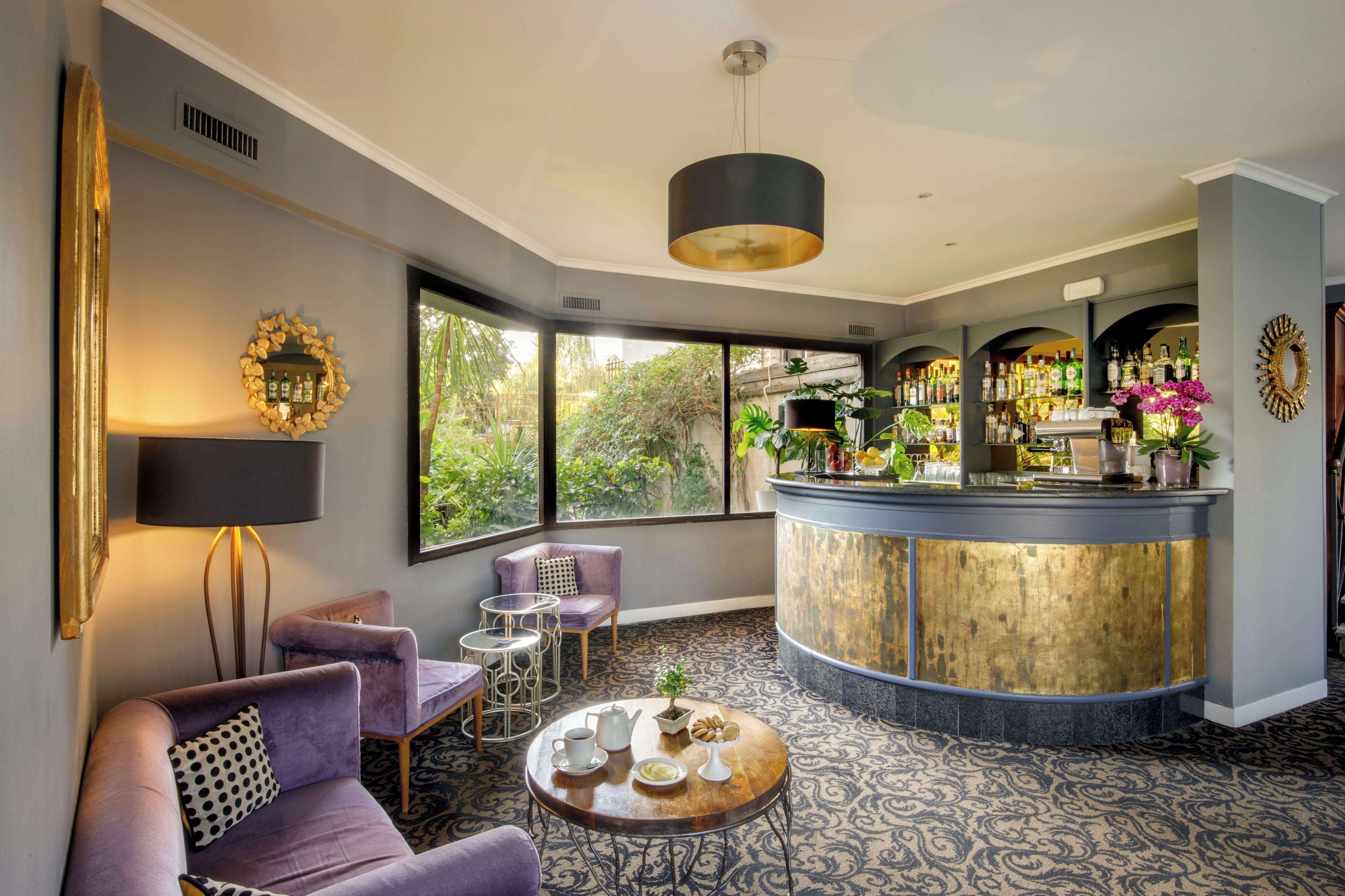 A bar area with a curved counter, seating with round tables, and a view of greenery outside.