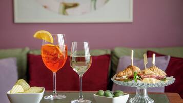 Un tavolo da pranzo con un bicchiere di bevanda rossa, un bicchiere di bevanda trasparente, un piatto di panini e ciotole di patatine e olive.
