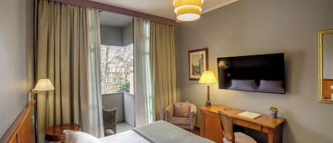 Una habitación de hotel con una cama, un escritorio, una silla, un televisor y una ventana con cortinas.