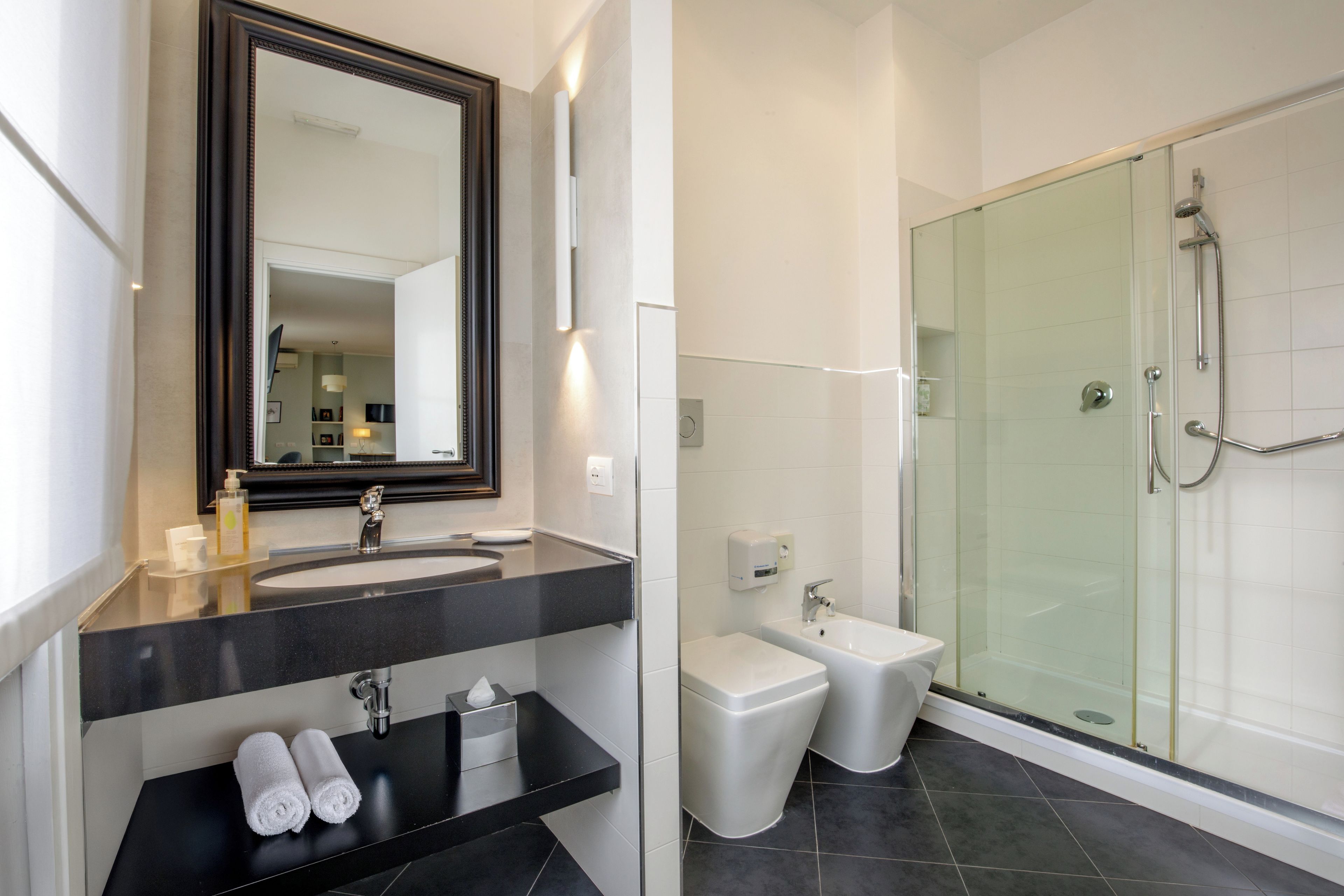 Ein modernes Badezimmer mit großem Spiegel, schwarzem Waschtisch, Bidet und einer Duschkabine.