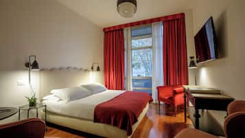 Ein Hotelzimmer mit Bett, Schreibtisch, Stuhl, Fernseher und einem Fenster mit Vorhängen.