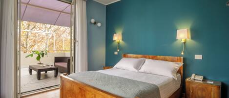 A hotel room with a wooden bed, a small bedside table, a nightstand with a phone, and a view of the outdoors through a sliding glass door.