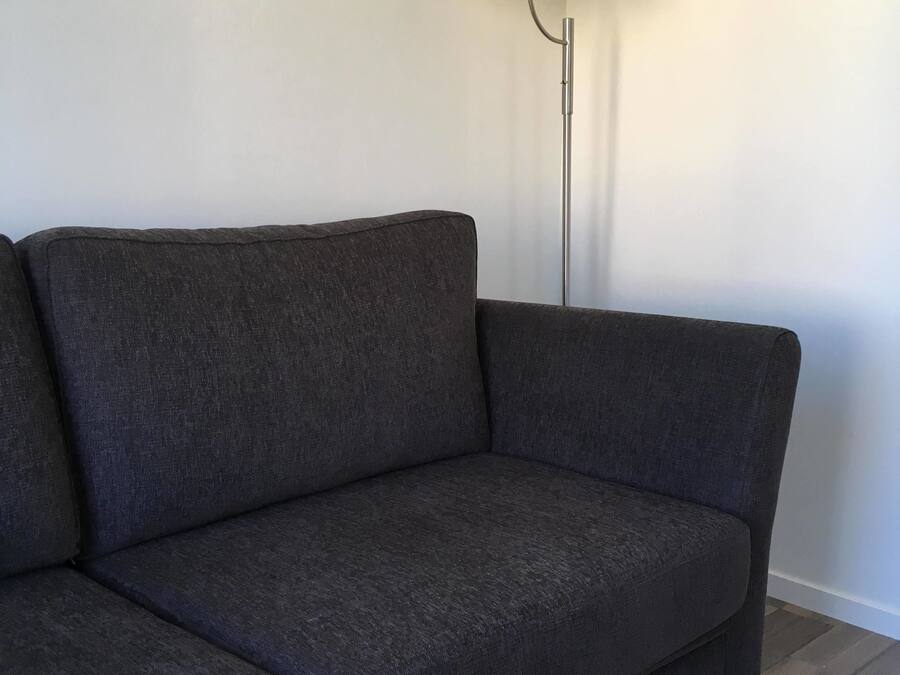 Tummanharmaa sohva tavallista seinää vasten, ja sen vieressä valkoinen lattiavalaisin.