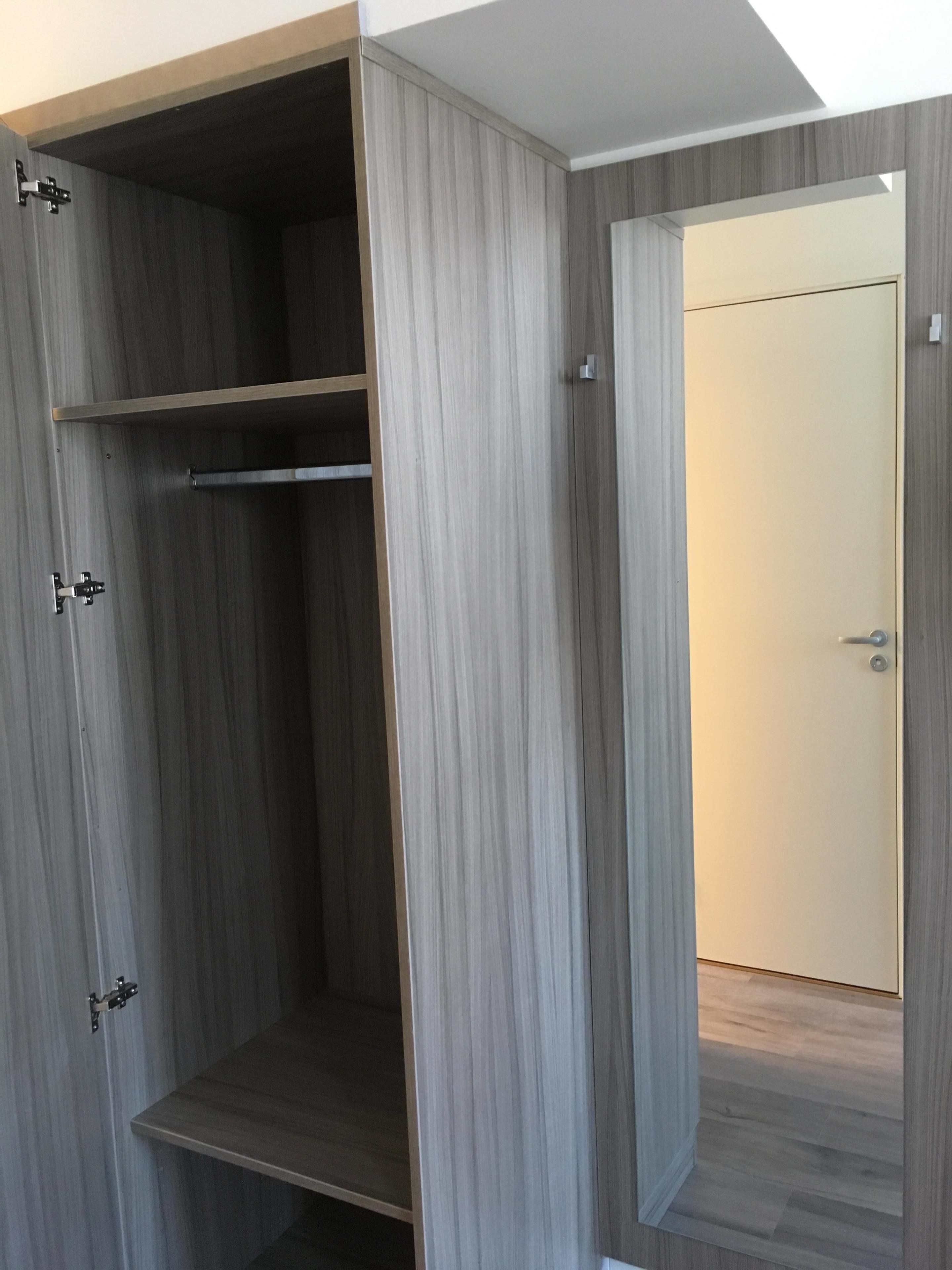 A walk-in closet with a wooden finish and a mirrored closet door.
