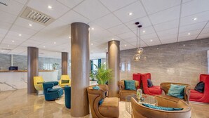 Un hall d'entrée moderne avec de hauts plafonds, de grandes colonnes et différents espaces de détente, notamment des canapés et des fauteuils.