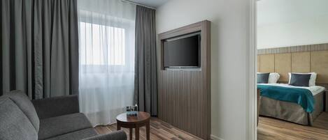 Habitación de hotel con sofá, una mesita, televisión montada en la pared y cama con cabecero.
