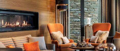 Una sala de estar moderna con chimenea, dos sillones, un sofá y una mesa de centro.