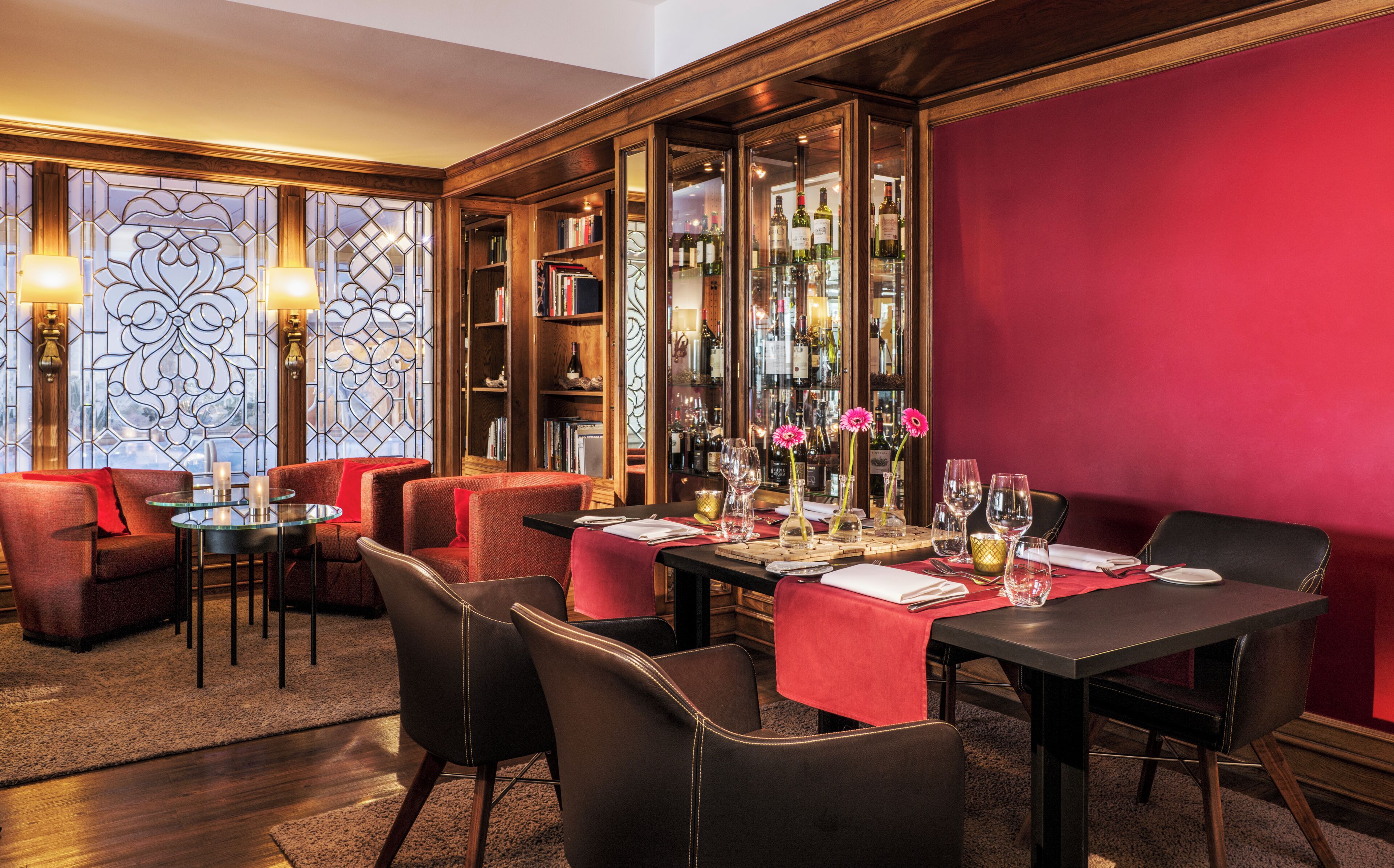 Comedor con una mesa roja, sillas negras y una exhibición de vinos.