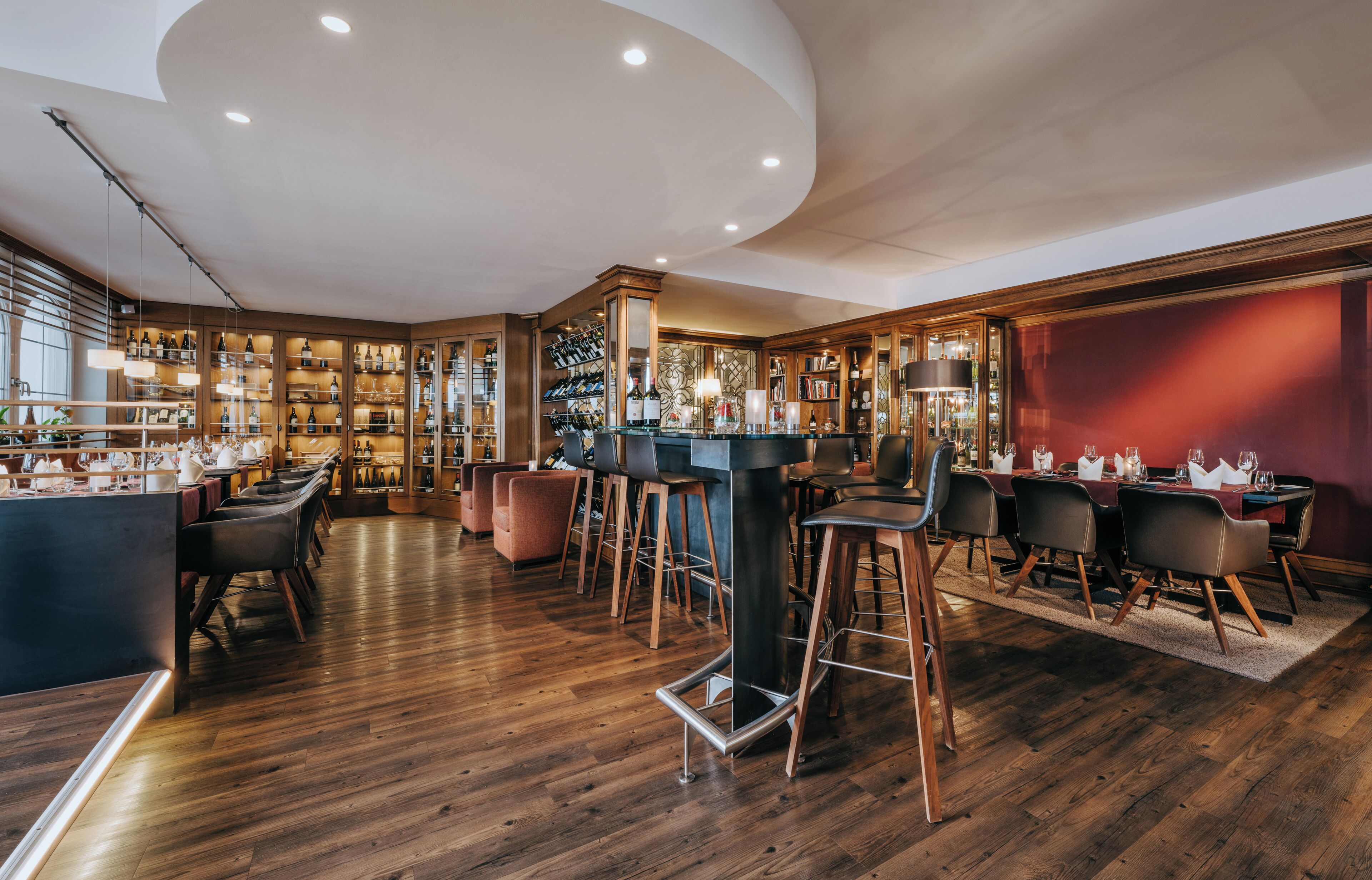A modern bar area with wooden flooring, bar stools, and a wine rack.
