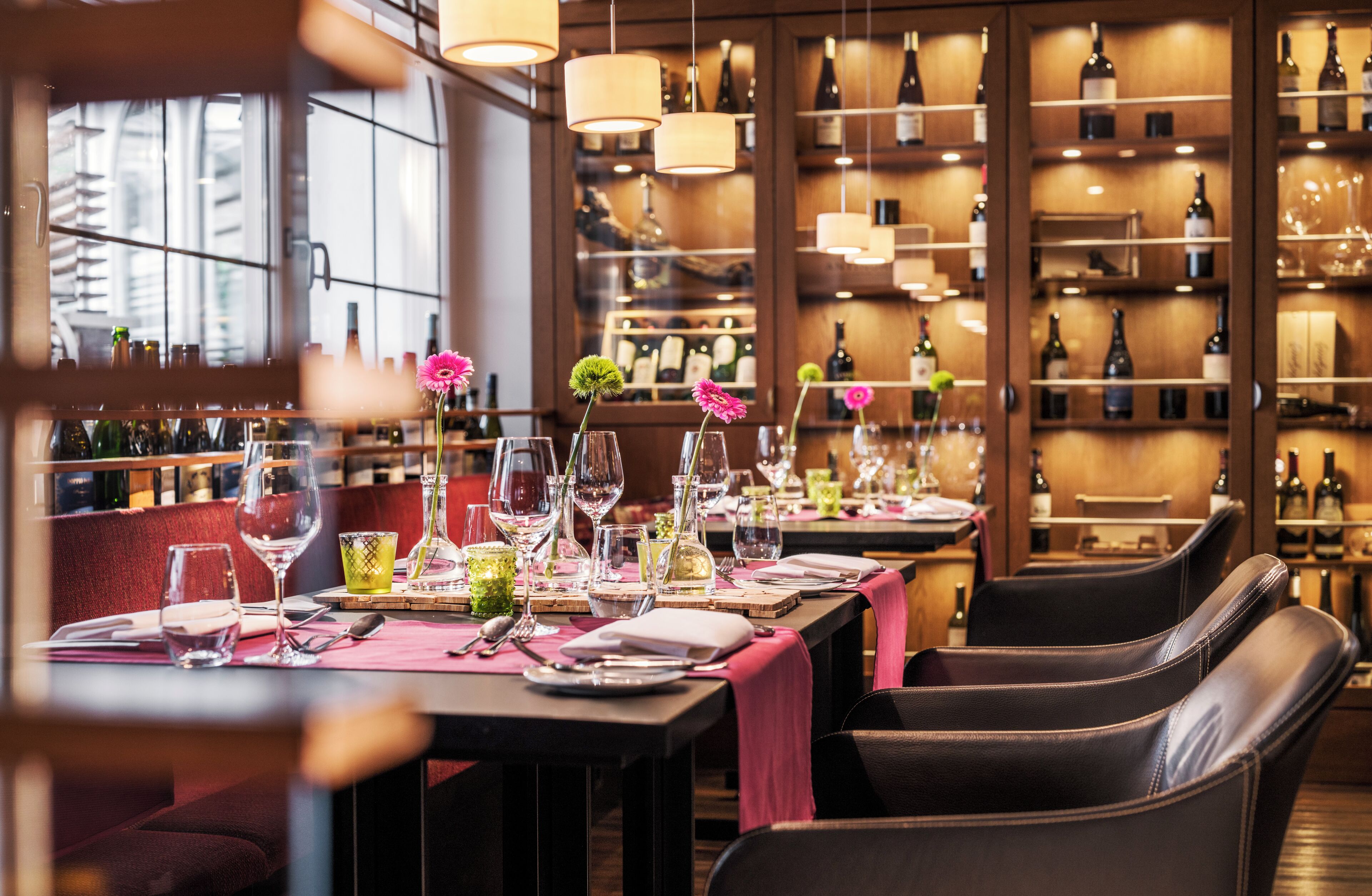 A restaurant with tables set for dining, wine bottles on shelves, and hanging lights.