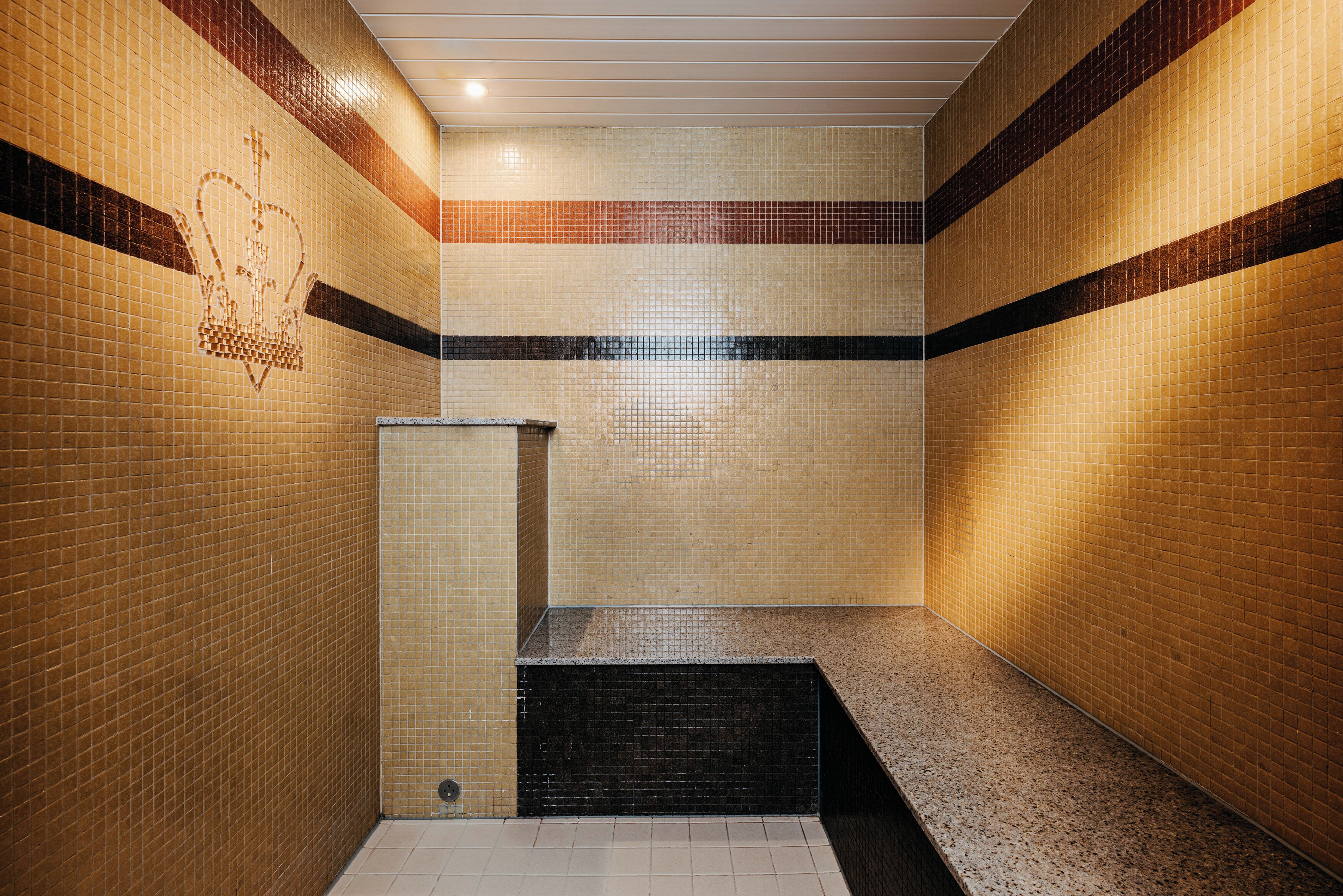 A tiled bathroom with a crown symbol, a sink, and a bench.