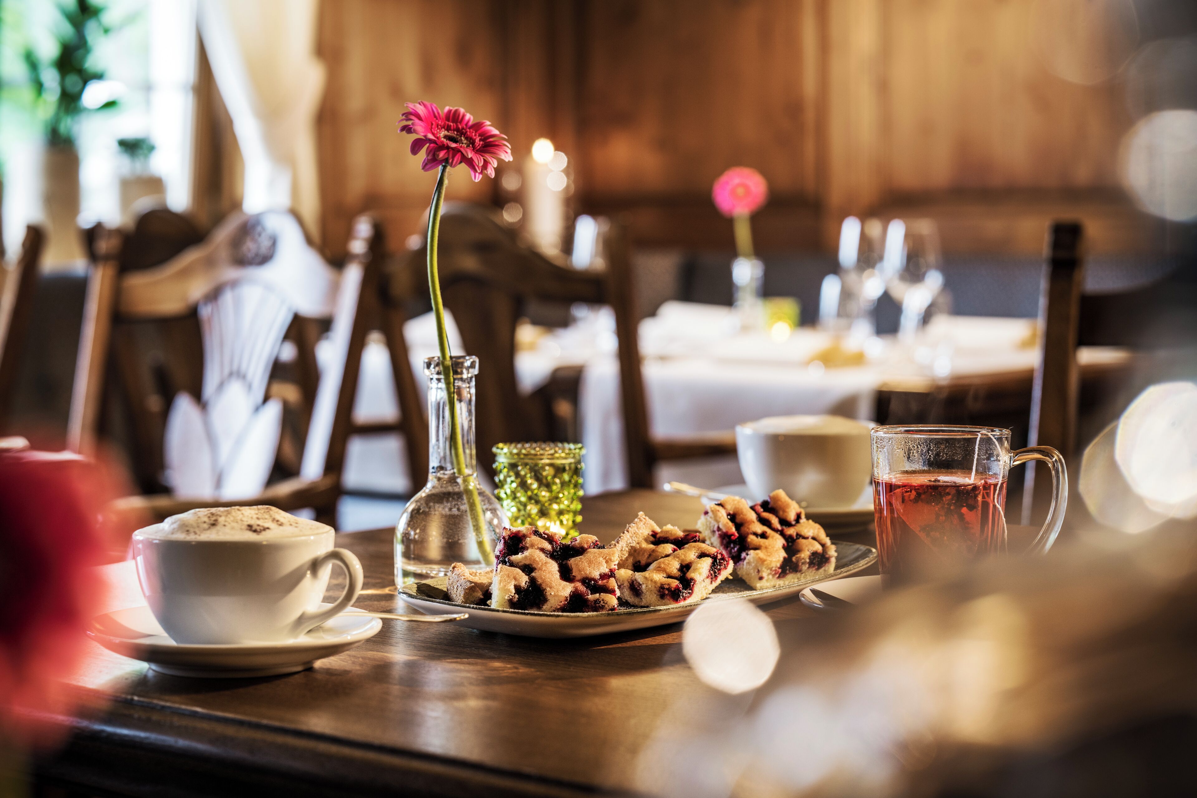 A dining table with a cup of coffee, a glass of water, a plate of cookies, and a vase with a flower.