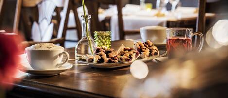 A dining table with a cup of coffee, a glass of water, a plate of cookies, and a vase with a flower.