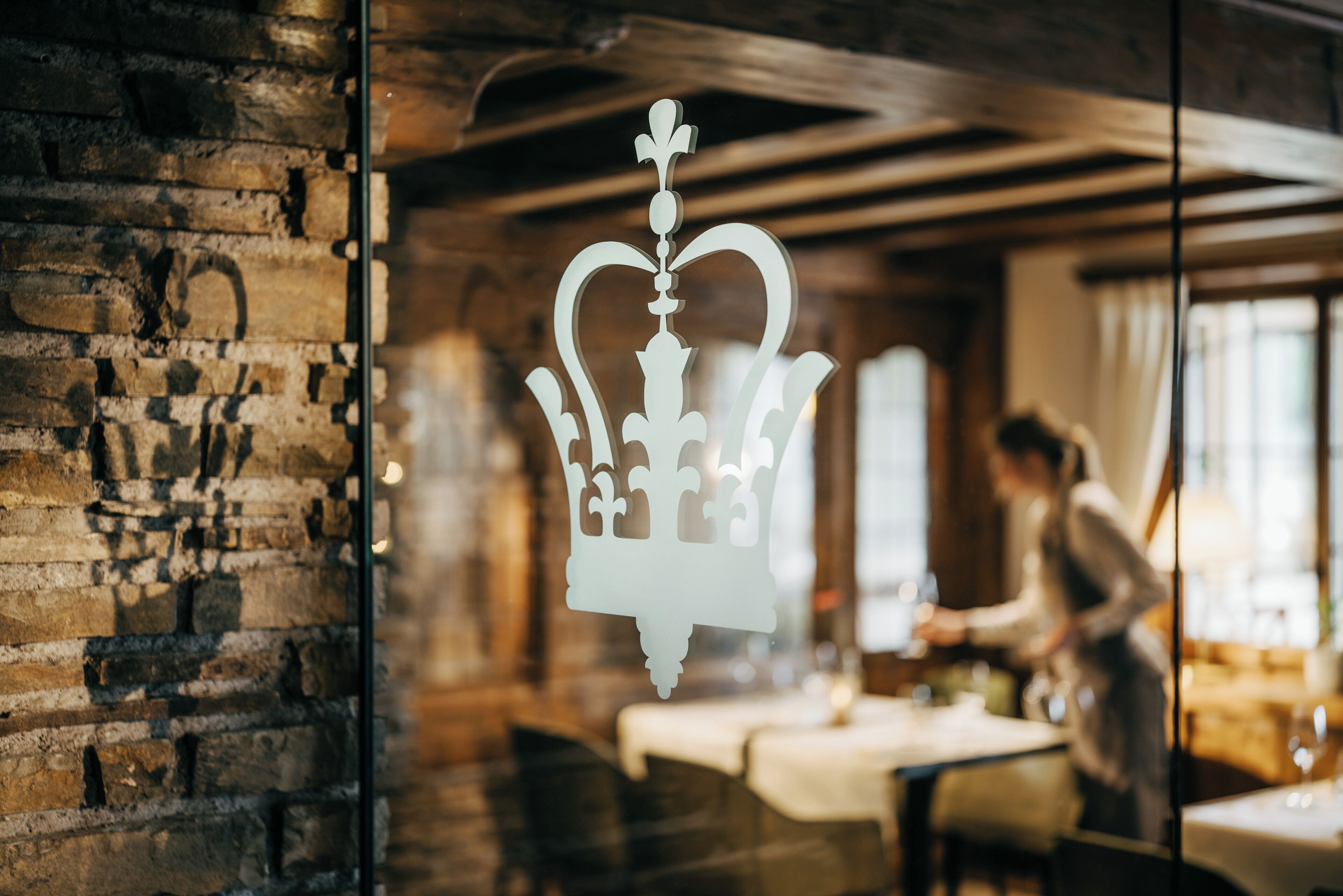 Een restaurant interieur met een bakstenen muur, een kroonvormige decoratie en een eethoek met tafels en stoelen.
