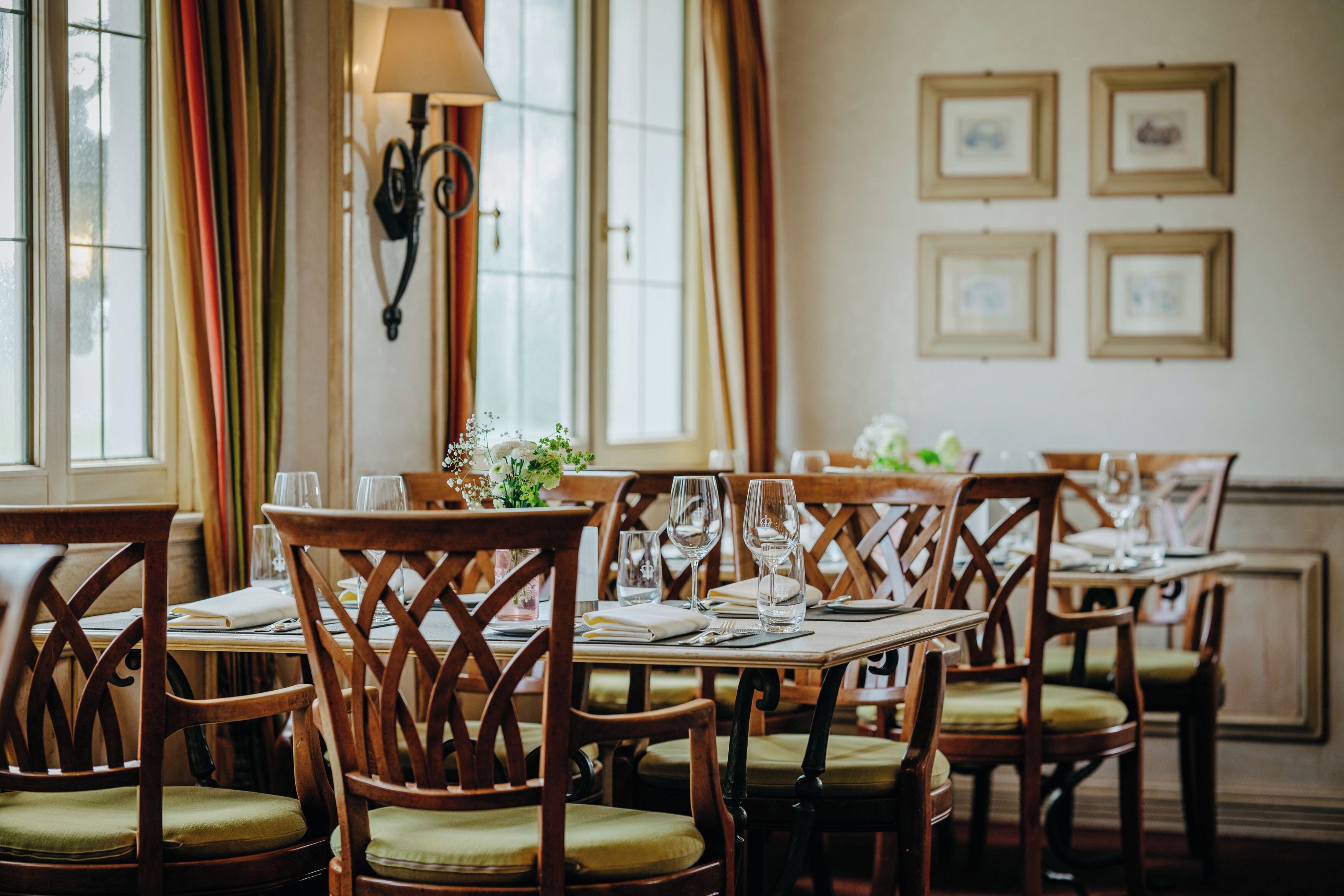 A dining area with wooden chairs and tables, a lamp, and framed pictures on the wall.