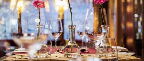 A dining table with clear glass vases containing pink flowers, surrounded by wine glasses and a wooden table runner.