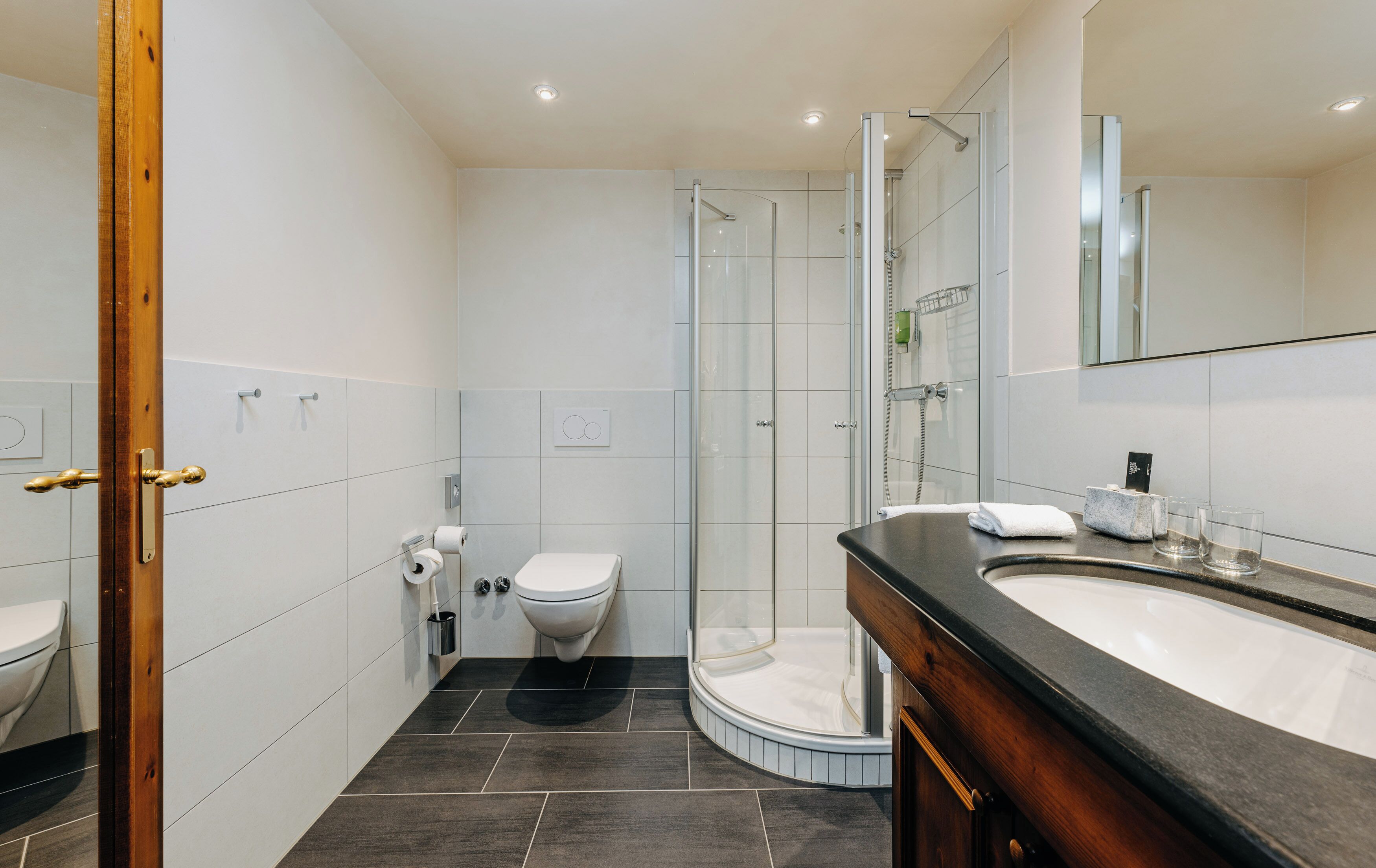 Een moderne badkamer met toilet, bidet, glazen douchecabine en een wastafel met spiegel.