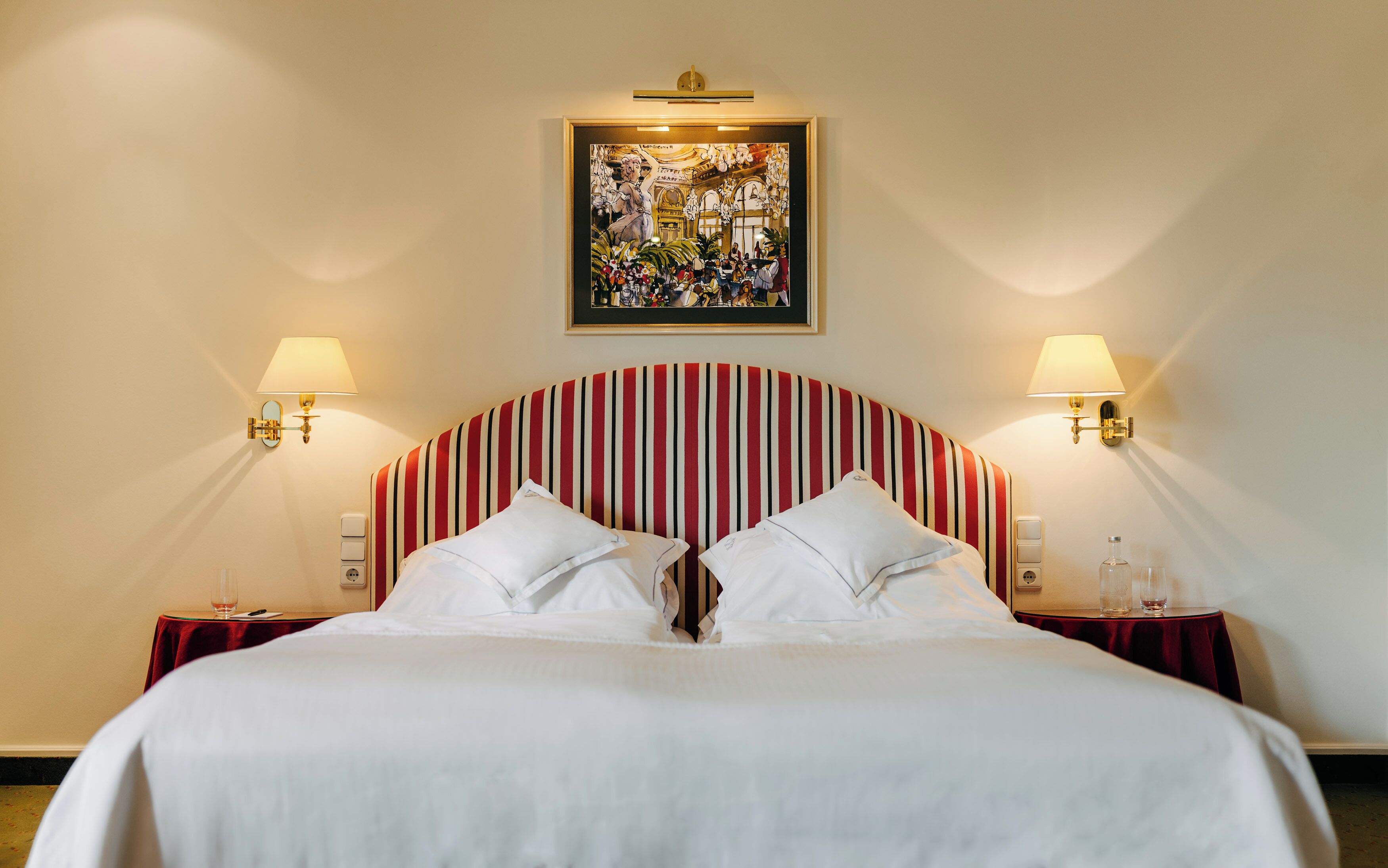 A hotel room with a large bed, two bedside tables, a wall-mounted painting, and two wall-mounted lamps.