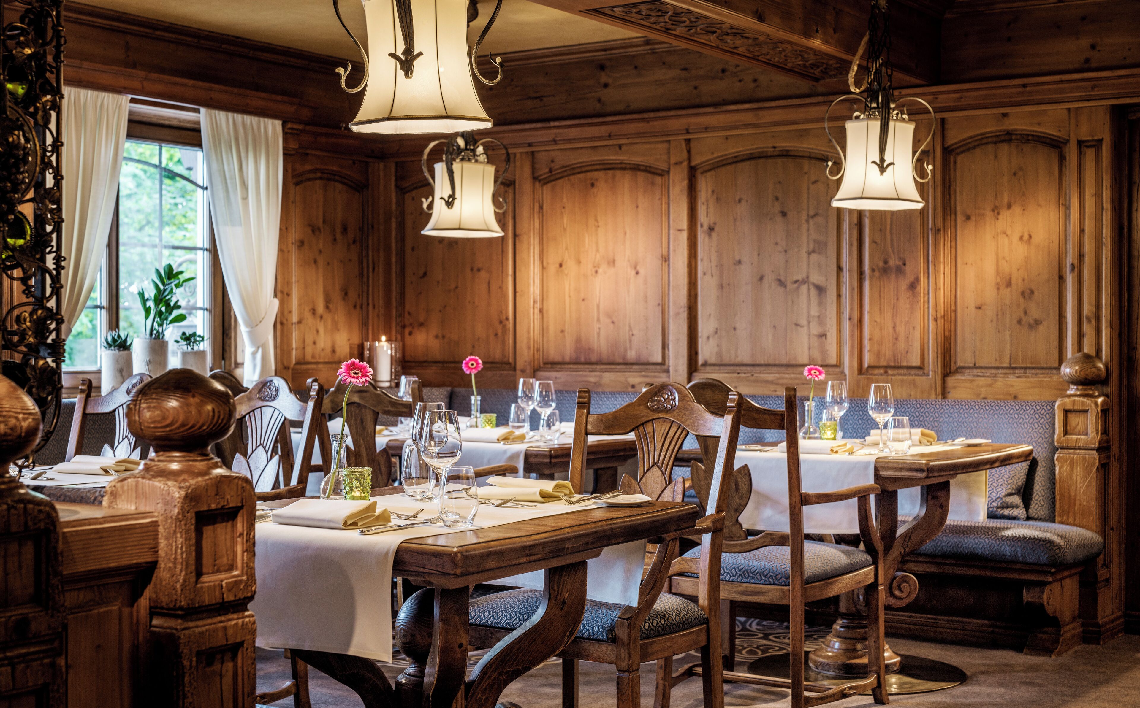 A wooden dining room with tables set for a meal, chairs, and hanging light fixtures.