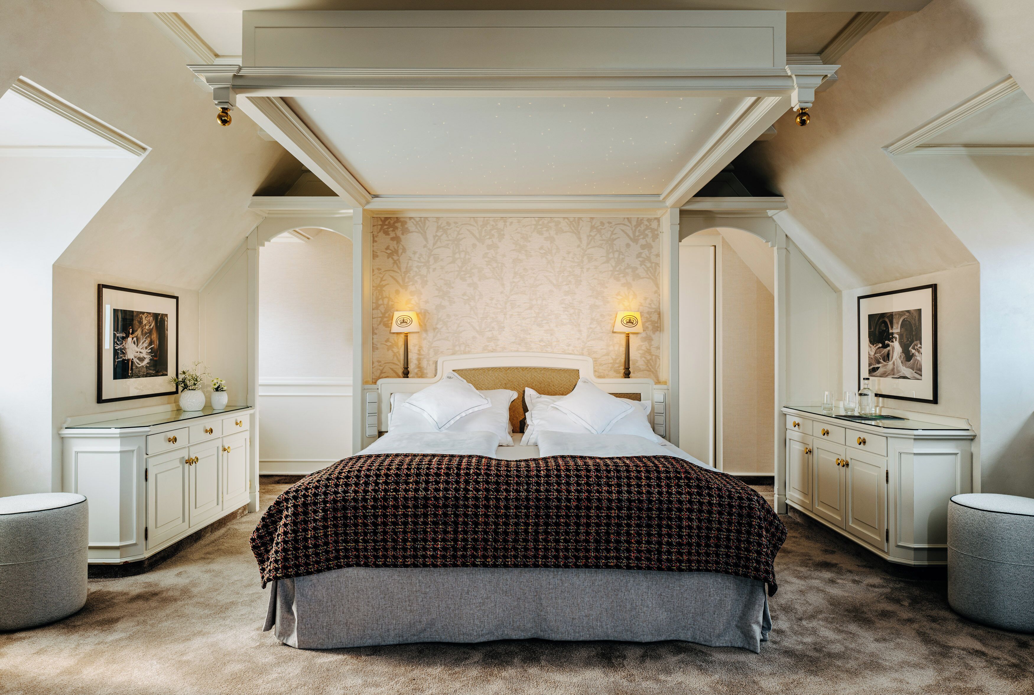 A bedroom with a large bed, two bedside tables, a dresser, and a ceiling with a skylight.