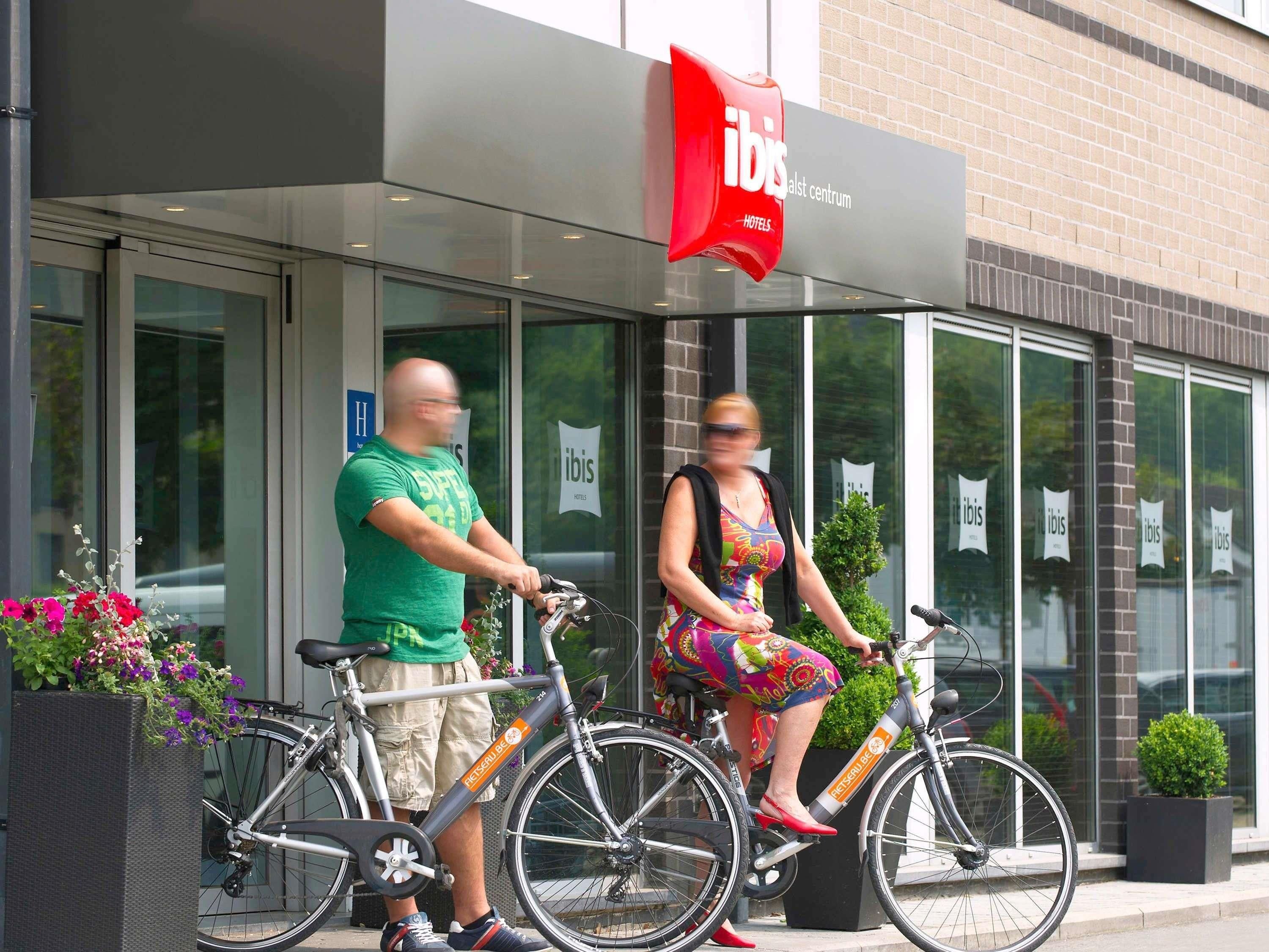 A hotel entrance with a red sign, glass doors, and two bicycles parked outside.