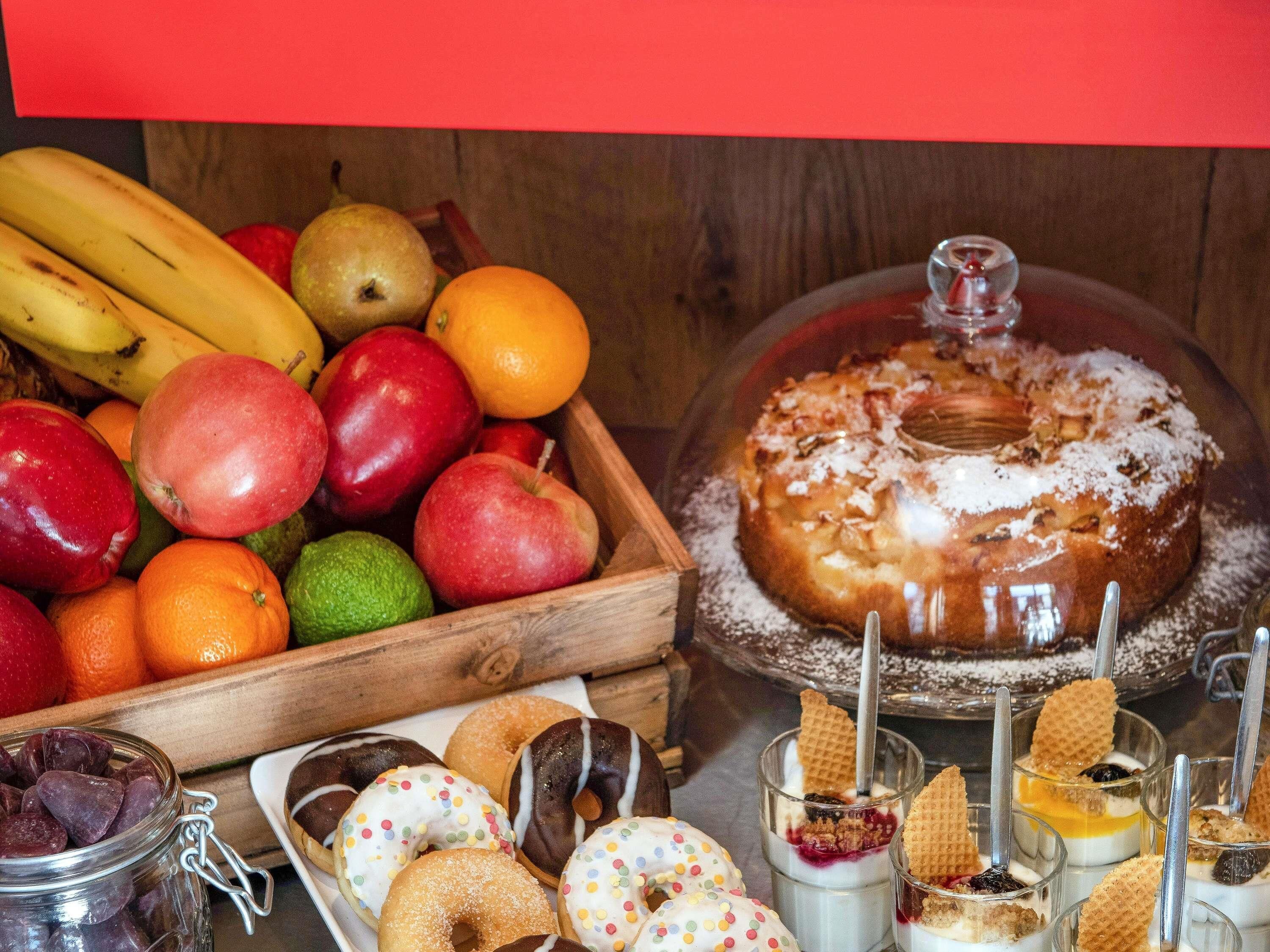 Een houten kist vol fruit, een taart met deksel op een presentatietafel en diverse desserts.