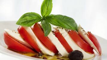 Une assiette blanche sur laquelle sont disposées des tranches de mozzarella et de tomates, garnies de feuilles de basilic.