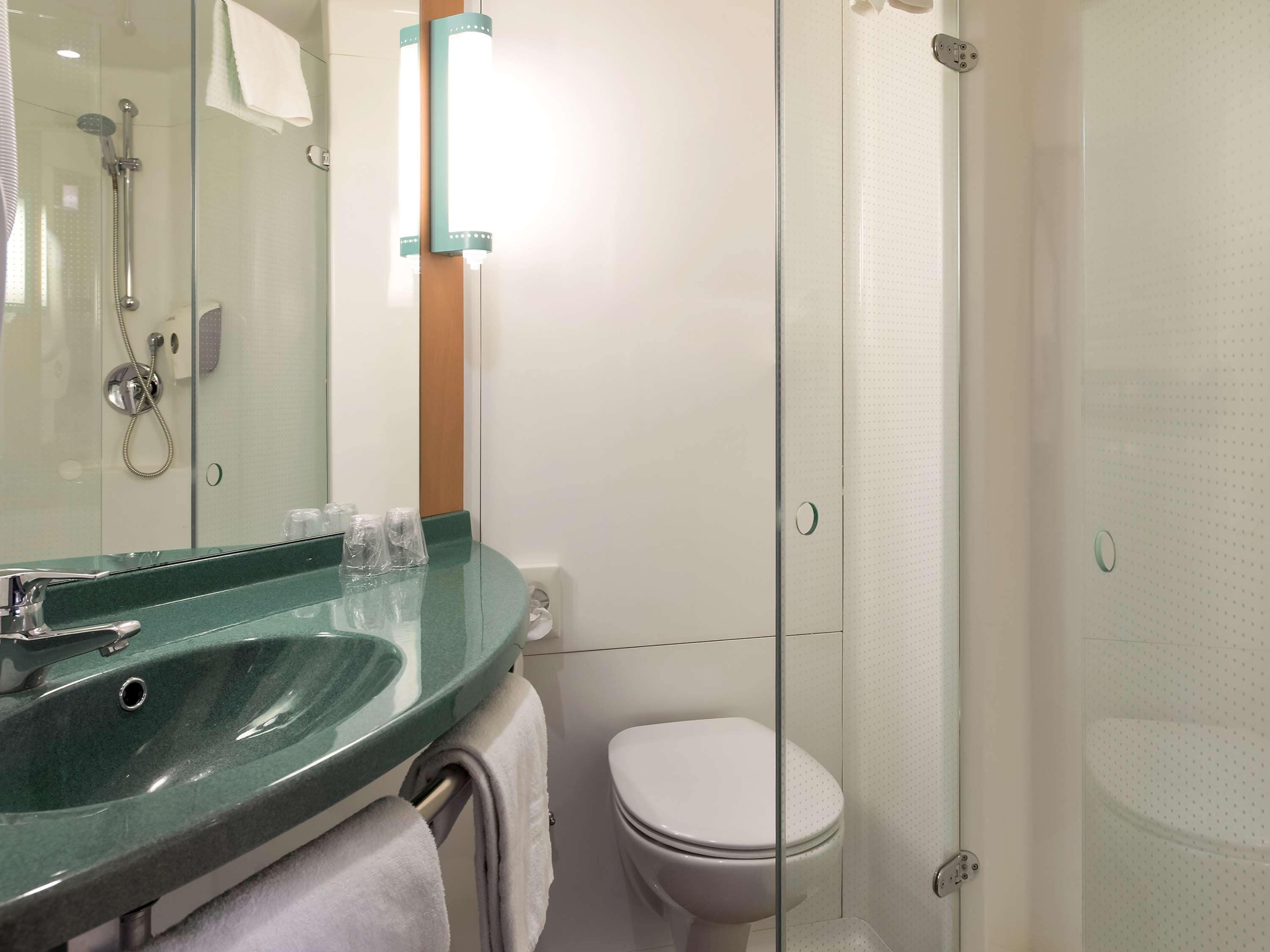 A modern bathroom with a glass shower enclosure, a green sink, and a white toilet.