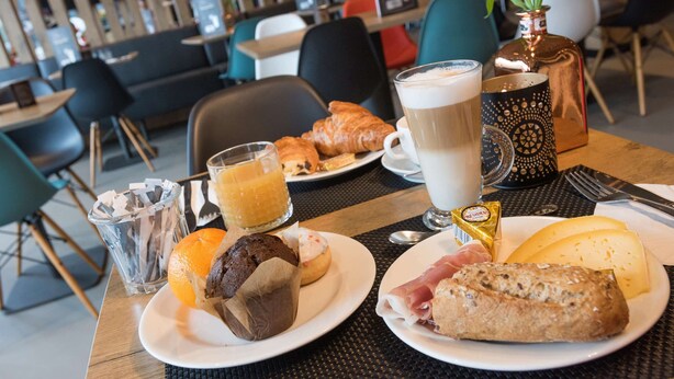 A breakfast setting with croissants, a muffin, a croissant sandwich, a glass of orange juice, a glass of coffee, and a small chocolate bar. - ibis Aalst Centrum (Aalst)