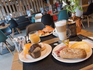 A breakfast setting with croissants, a muffin, a croissant sandwich, a glass of orange juice, a glass of coffee, and a small chocolate bar. - ibis Aalst Centrum (Aalst)