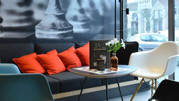 A modern interior with a large chess piece mural, a sofa with red cushions, and a round table with a vase.