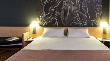 A hotel room with a large bed, two bedside lamps, a nightstand, a magazine, and a wall art piece.