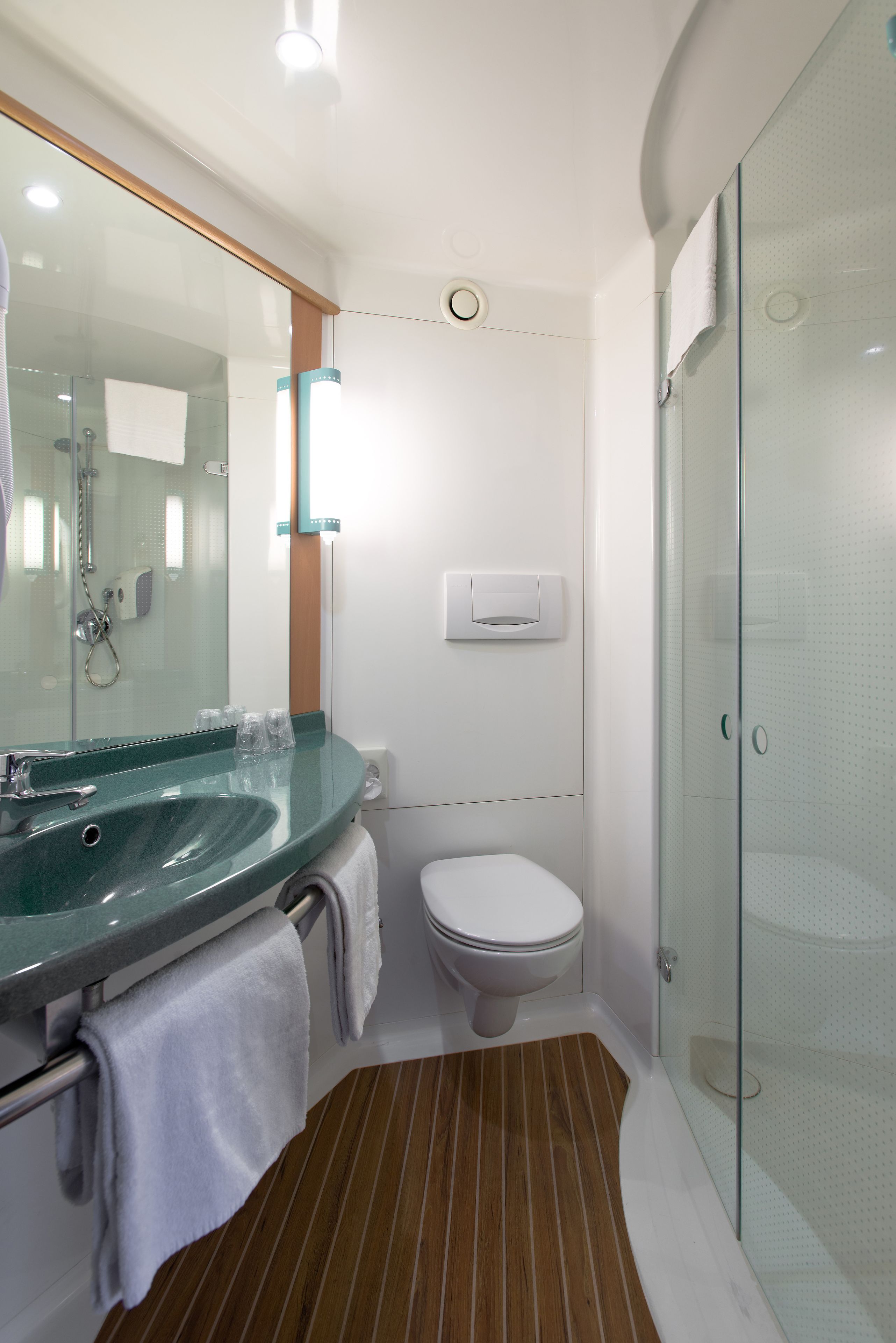 Une salle de bain moderne avec une douche à parois de verre, des toilettes blanches et un lavabo vert avec un miroir au-dessus.