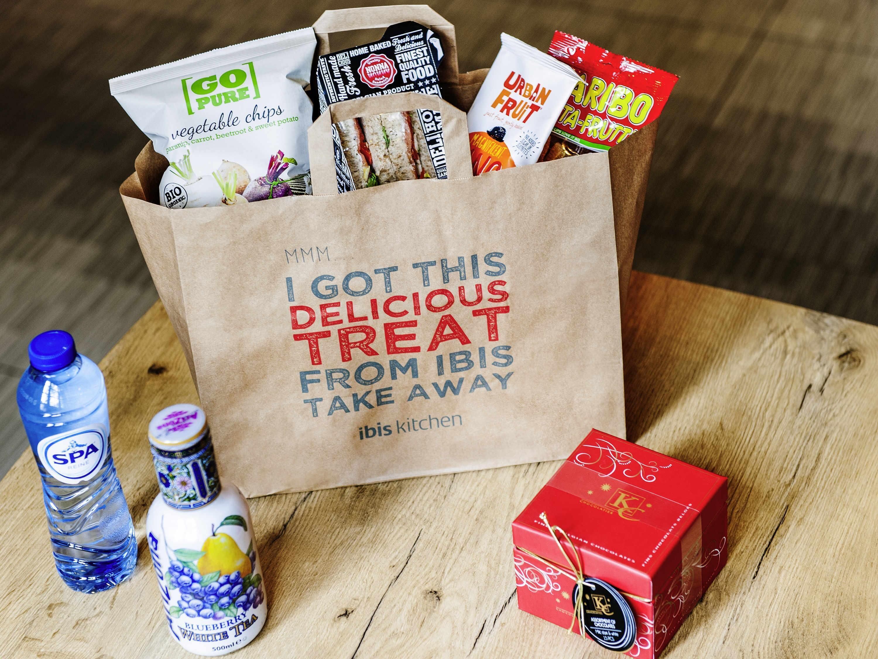 A paper bag filled with various food items and a bottle of water on a wooden surface.