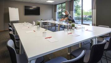 A conference room with a long table, chairs, a whiteboard, and a TV.
