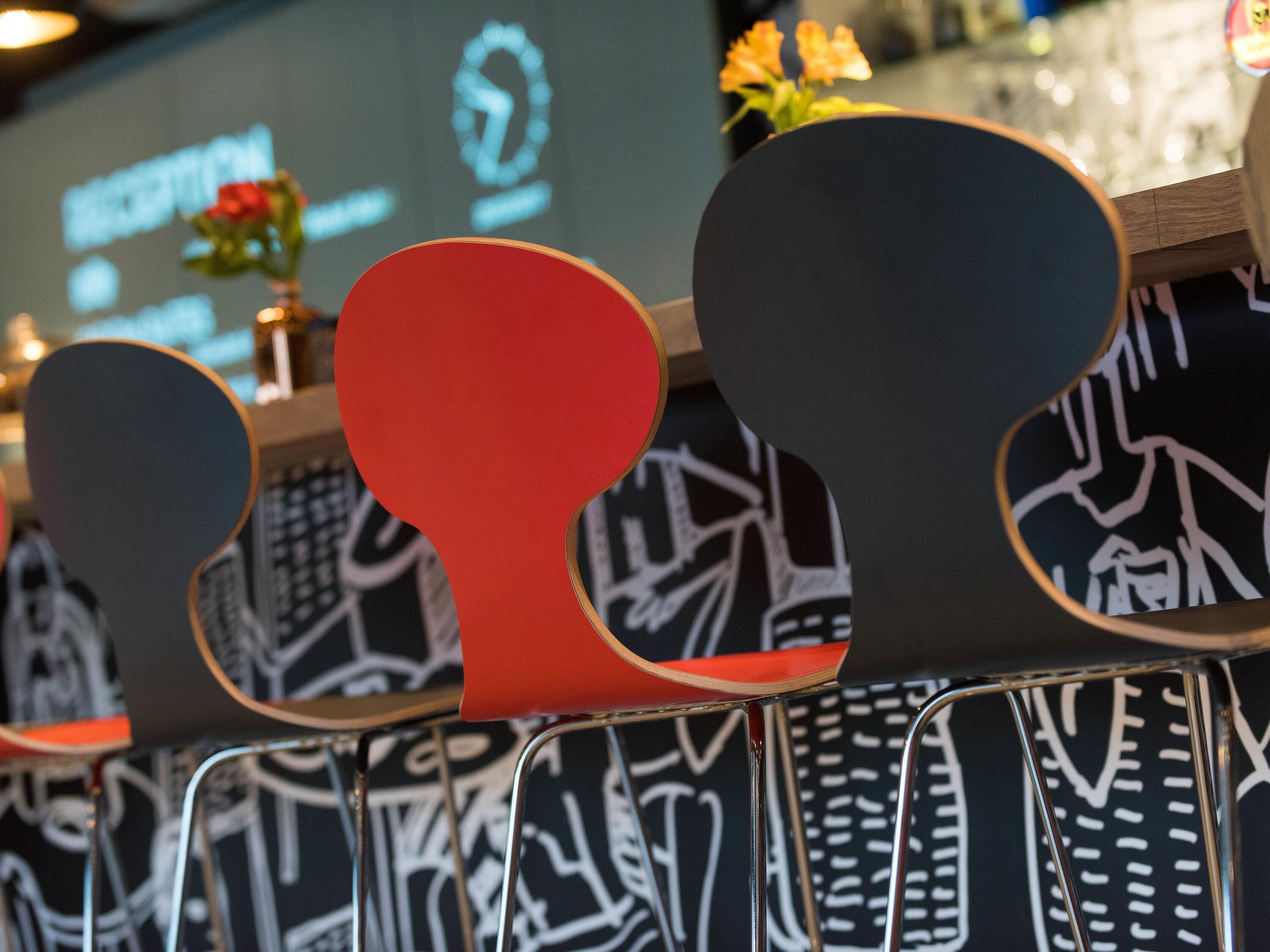 A row of chairs with a unique design, a black and white patterned wall, and a projection screen in the background.