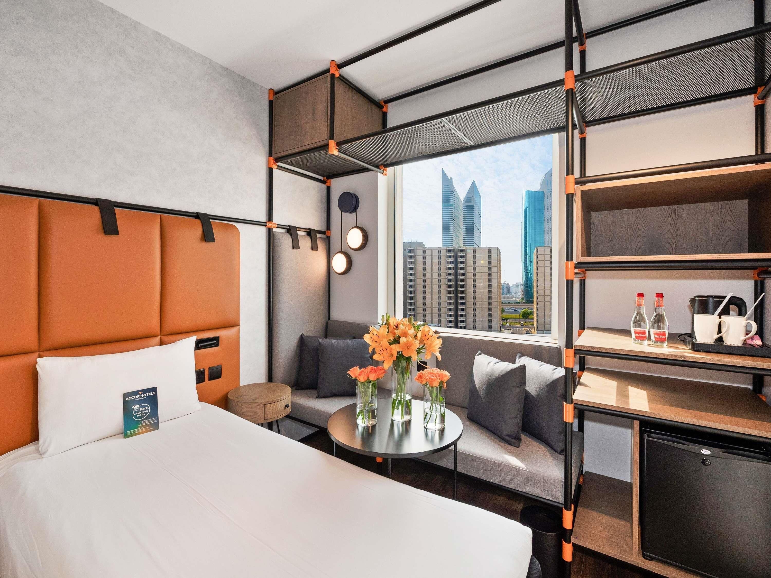 Una habitación de hotel moderna con cama, sofá, mesa redonda y un mini refrigerador.
