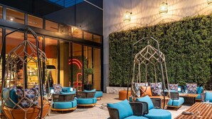 Un espacio exterior moderno con mobiliario de mimbre y cojines azules, una mesa de madera y una pared verde con plantas trepadoras.