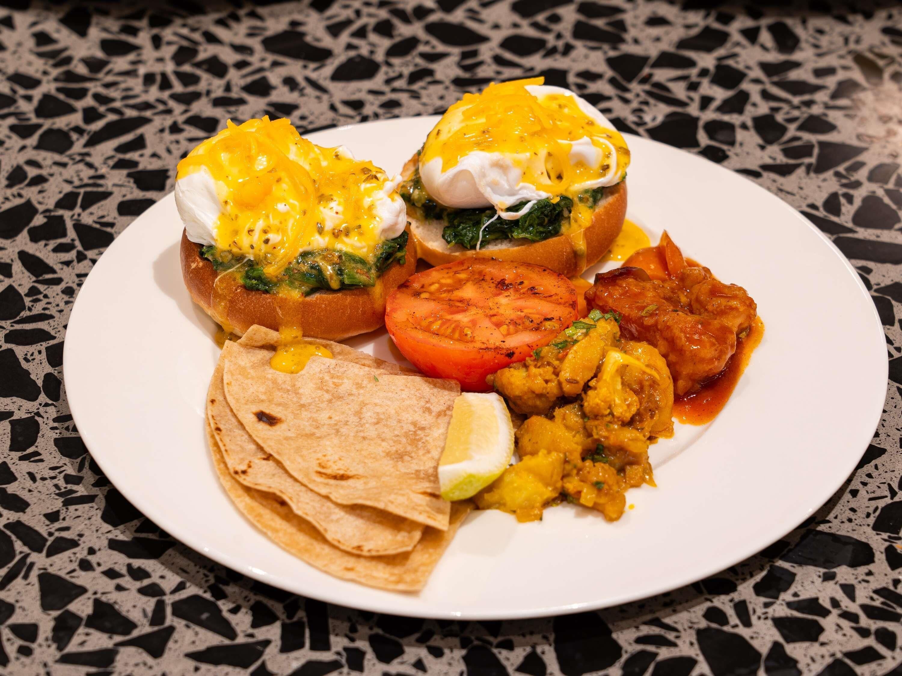 A plate of food with eggs benedict, a tomato slice, and a side of curry.