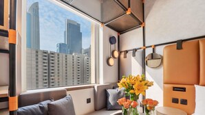 Una habitación moderna con vista a la ciudad, un sofá, una mesita con jarrones y una cama con cabecera.