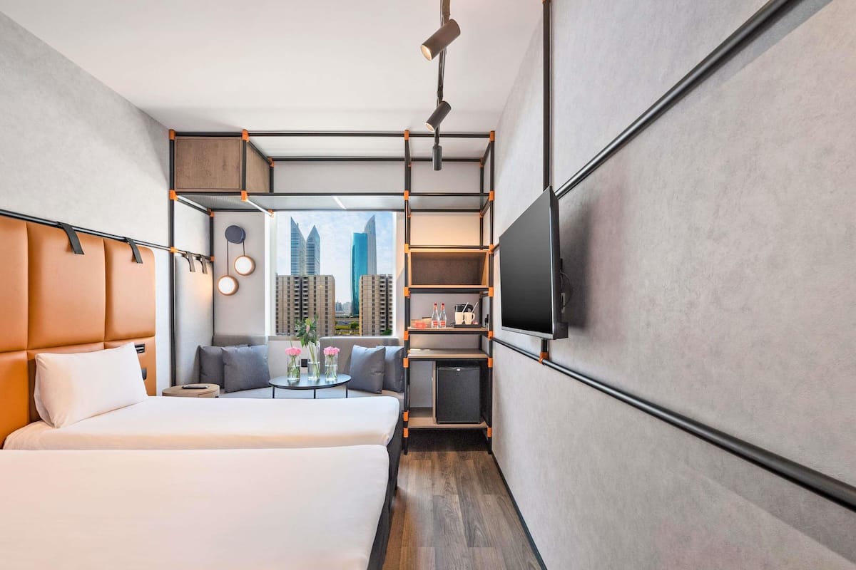 A modern hotel room with a large bed, a seating area with a table, a TV, and a city view.