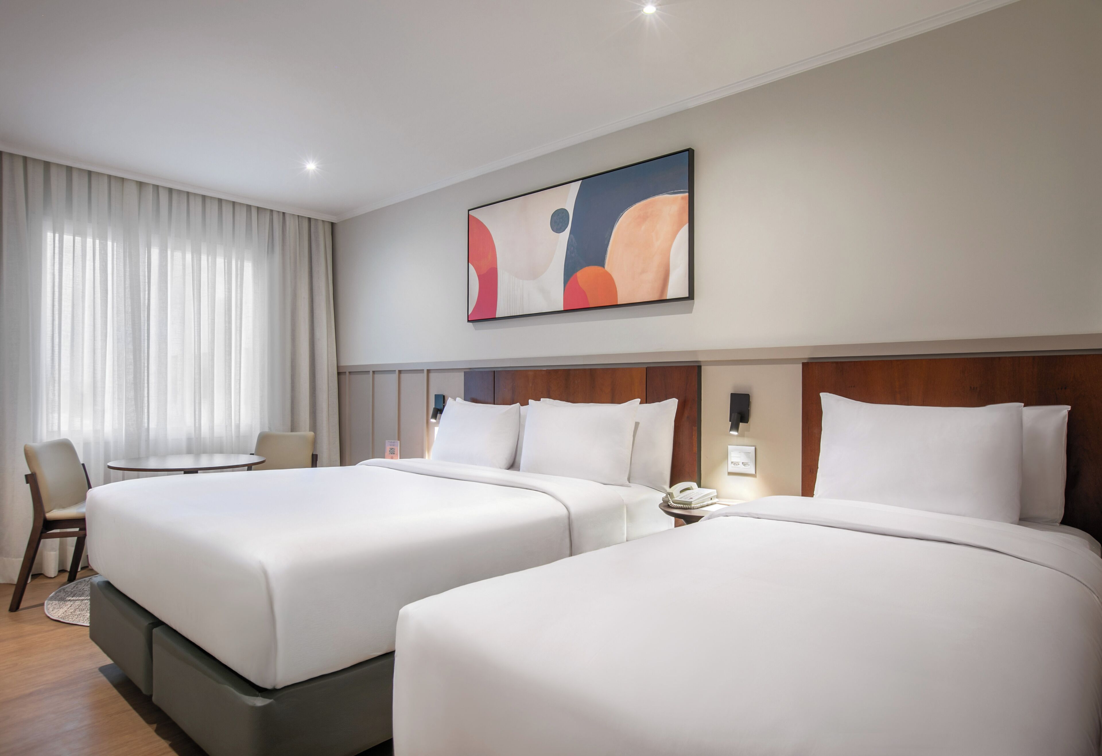 A hotel room with two beds, a desk, a chair, and a large abstract painting on the wall.