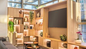 Una sala de estar moderna con un televisor grande, estanterías de madera con plantas y un sofá gris.