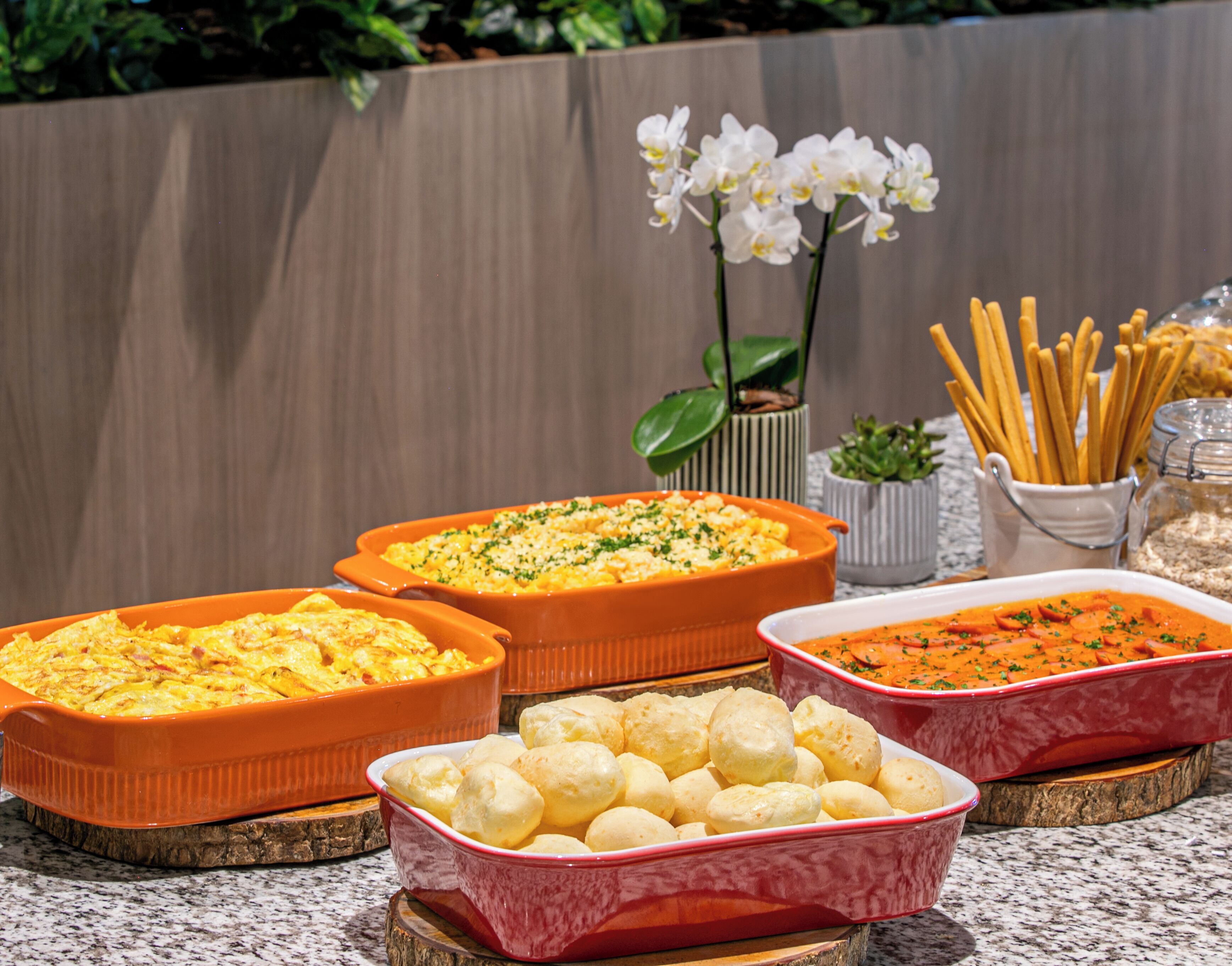 A buffet table with various dishes, including casseroles, bread rolls, and a dish with shredded carrots.